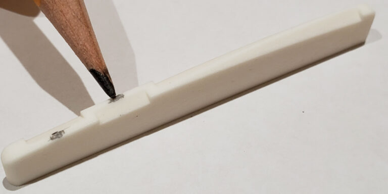 Using a pencil to add graphite to an acoustic guitar saddle.