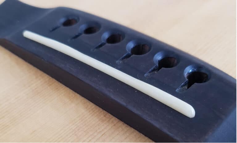 Close up of a bone guitar saddle on an acoustic guitar with no strings